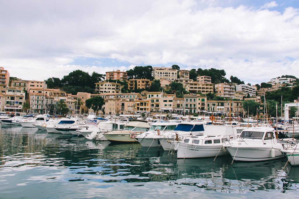 Boote liegen im Yachthafen von Puerto de Sóller vor Anker, mit Gebäuden und Häusern am Berghang auf Mallorca.